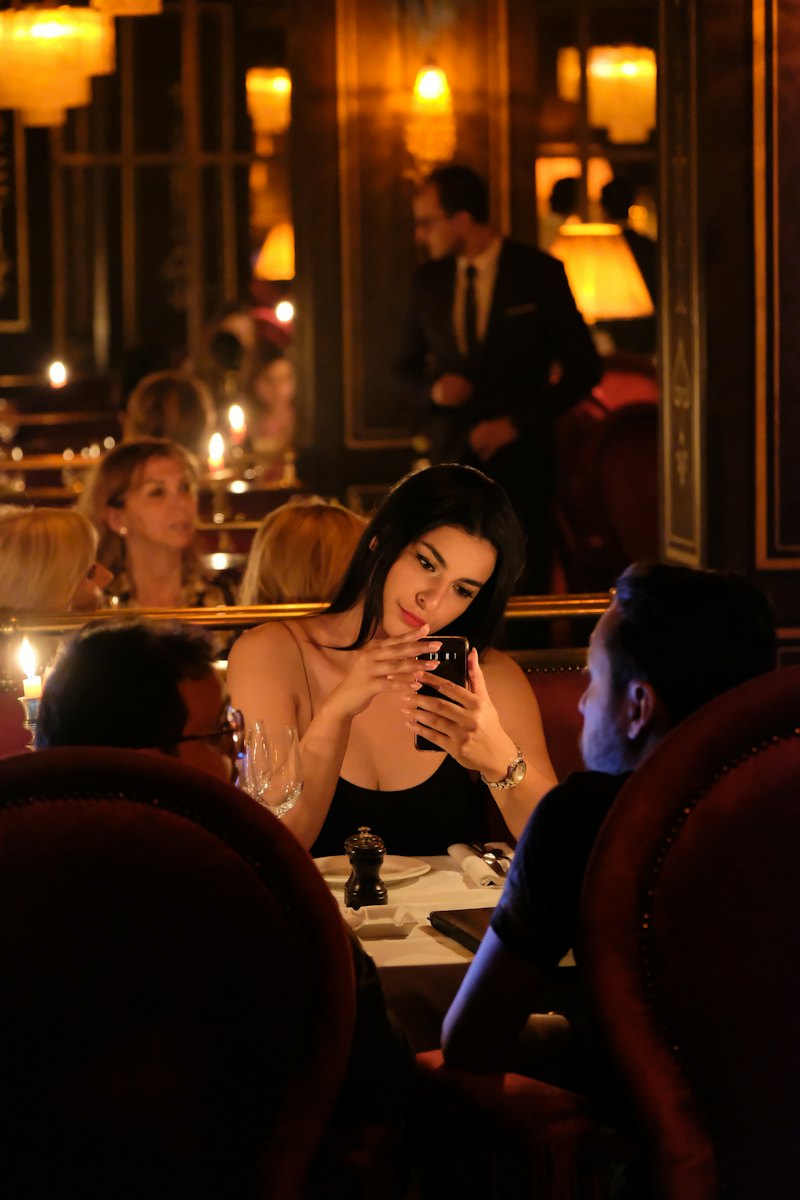 Mulher sorrindo enquanto olha o celular em um restaurante à meia-luz