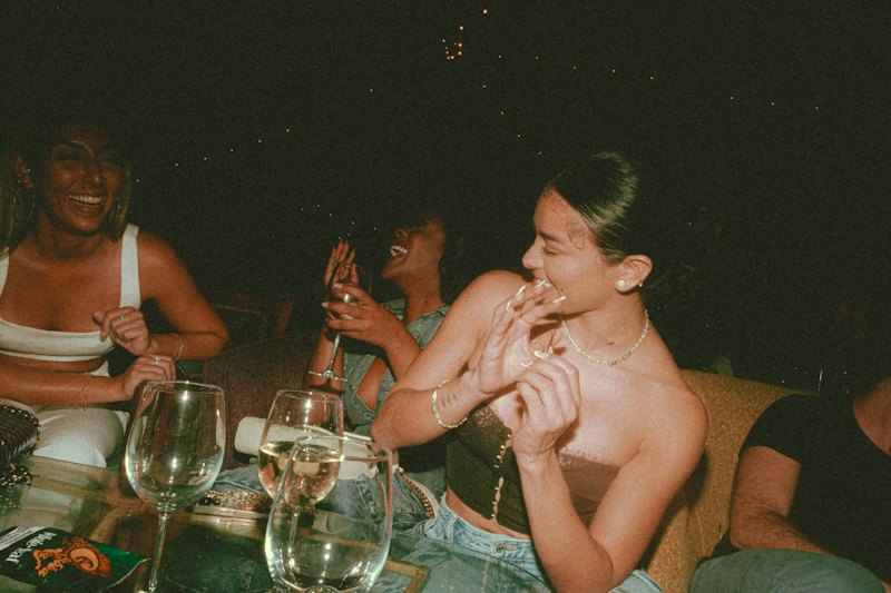 Amigas rindo à mesa com taças de vinho à noite